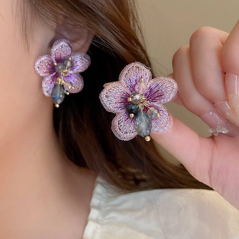 Close-up of personalized all-match flower ear studs with electroplated finish, delicate pink petals, and decorative gemstones worn by a woman