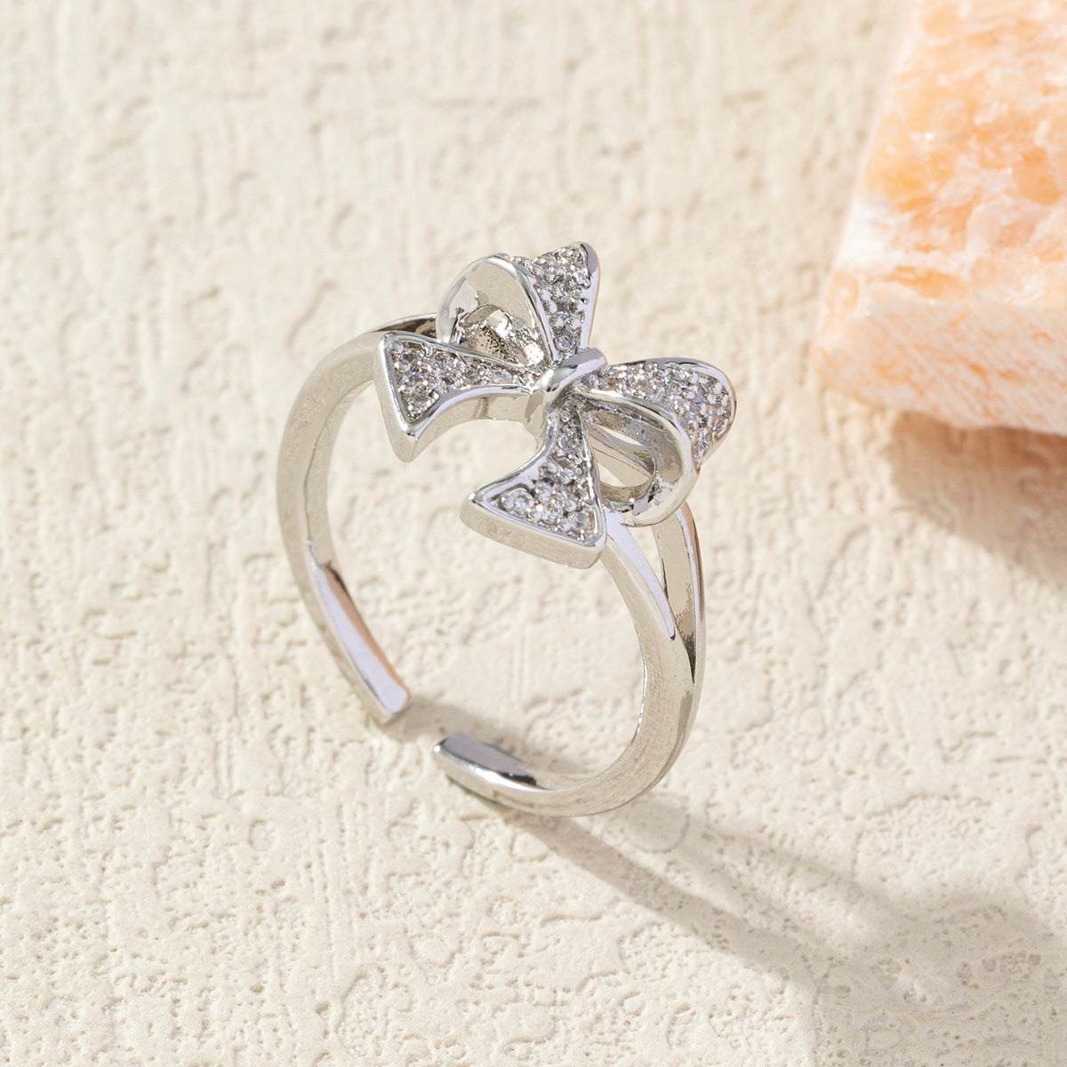 Diamond bow adjustable ring with copper plating and sparkling stones on textured background