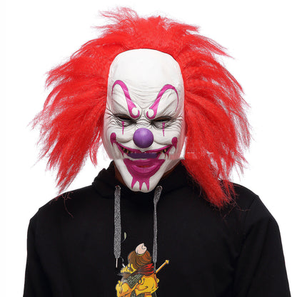 Front angled view of a person wearing a clown mask with red hair and a black hoodie on a white background