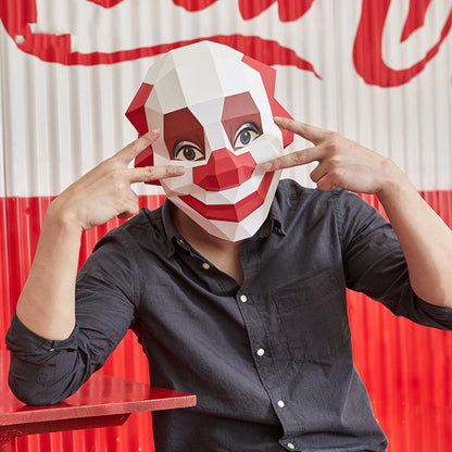 Person wearing a geometric clown mask in front of a Coca-Cola sign
